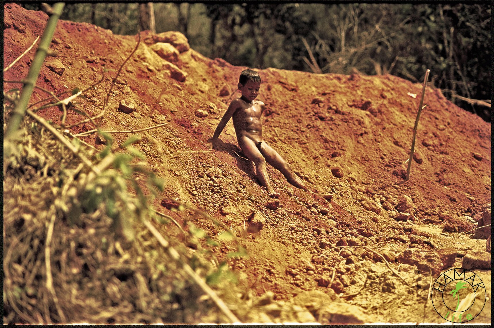 Zabawy kambodżańskich dzieci. Nagi chłopiec na piaszczystym zboczu.